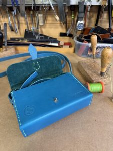 Bag in turquoise veg tan leather, hand stitched in bright green thread, lined with dark green nappa